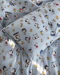 Light blue bedding set featuring a repeating cartoon print of Snoopy, Woodstock, and other Peanuts characters on the duvet cover and matching pillowcases.