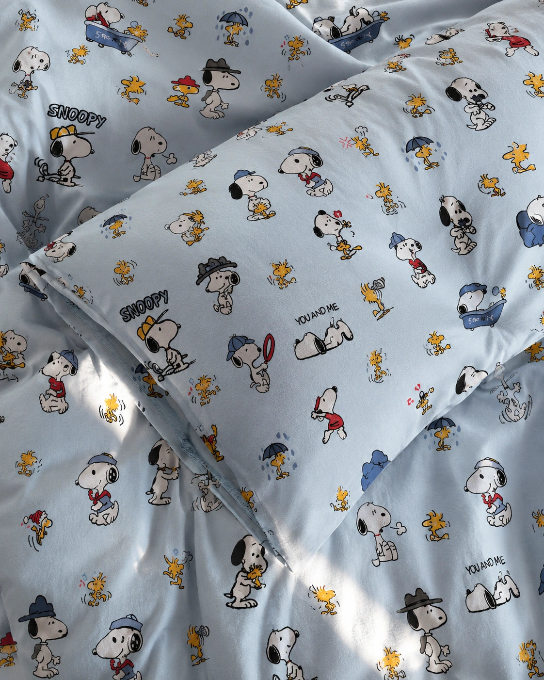 Light blue bedding set featuring a repeating cartoon print of Snoopy, Woodstock, and other Peanuts characters on the duvet cover and matching pillowcases.